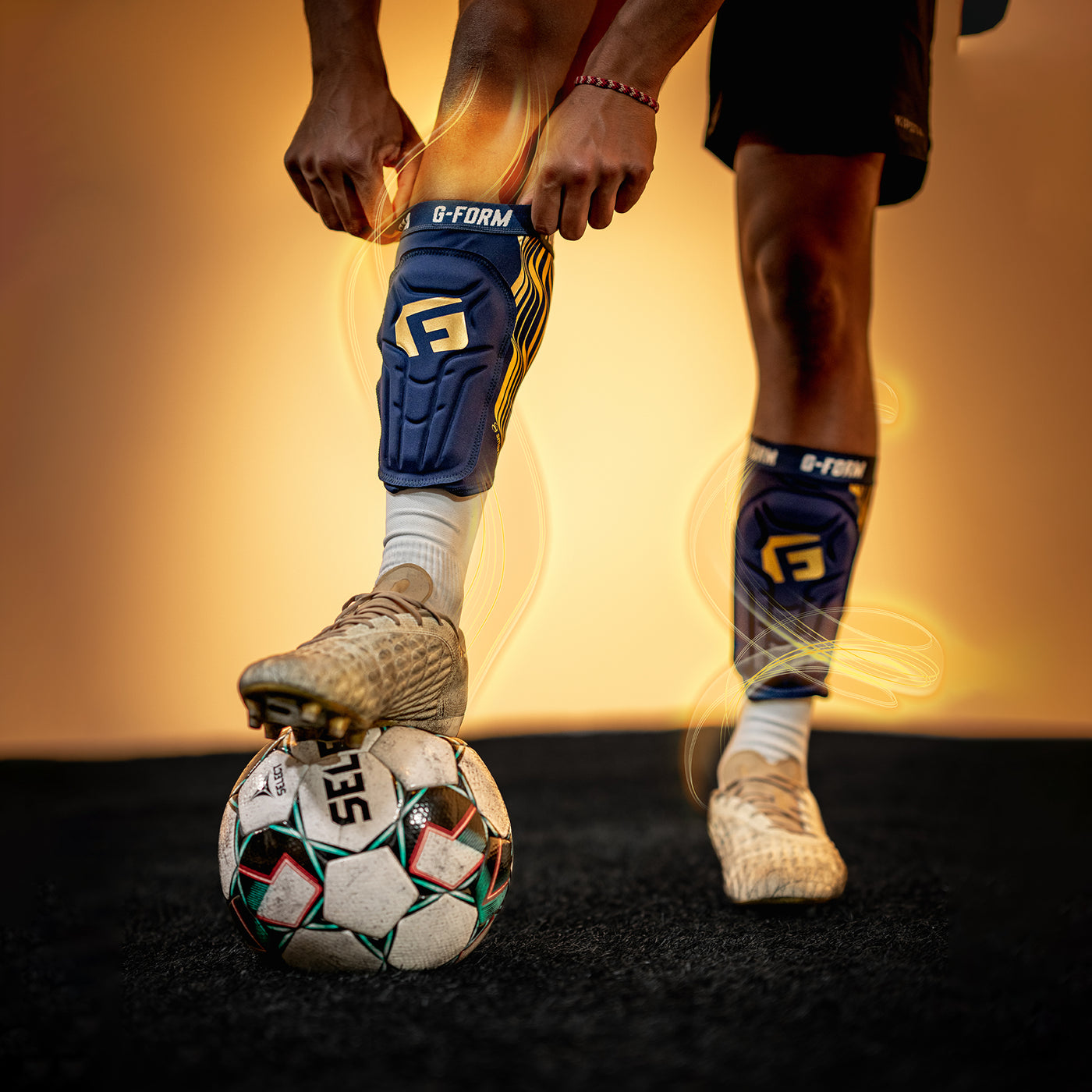 Person wearing G-Form knee pads and cleats with a soccer ball on a dark surface.