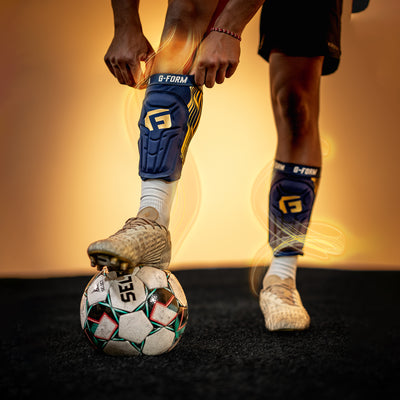 Person wearing G-Form knee pads and cleats with a soccer ball on a dark surface.