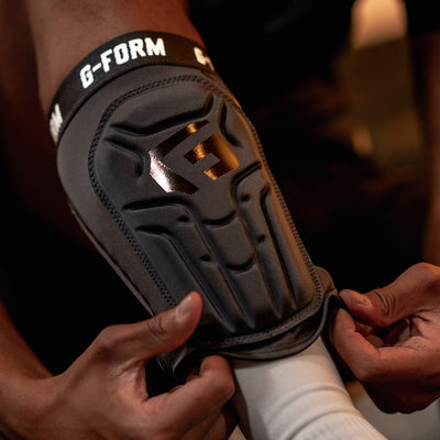 Black G-Form elbow pad being worn on a person's arm with a blurred background.