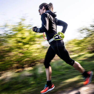 Woman running on a trail wearing the USWE Zulo Hydration System Waist Pack in bright yellow, highlighting the lightweight and secure fit designed for active runners. | 8Lines Shop